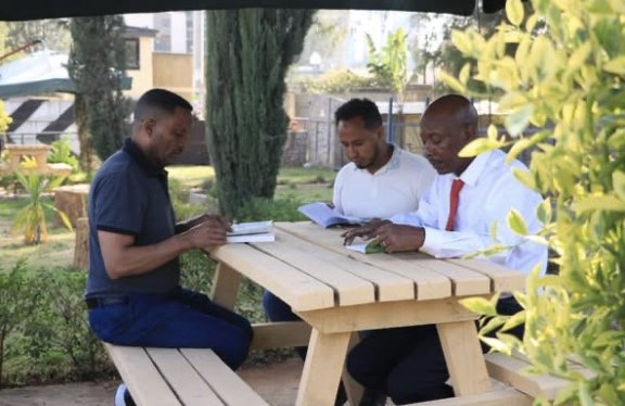 Three men reading together at a wooden picnic table in the book club garden