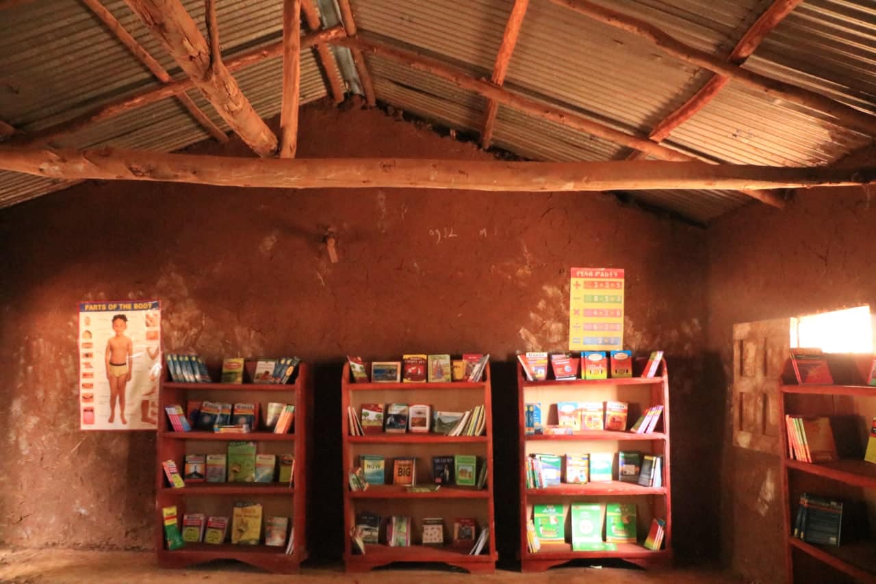 Red bookshelves full of books in a mud-walled classroom at Daro